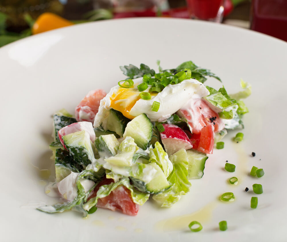 Homemade fresh vegetable salad with sour cream and poached egg