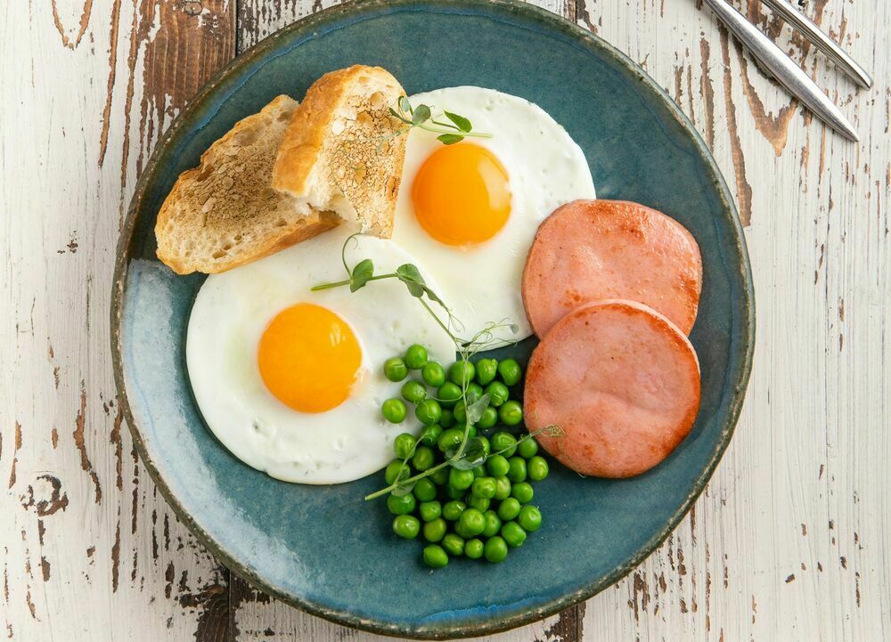 Fried eggs with fried sausage and green peas